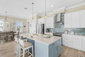 A modern kitchen with a central island, white cabinetry, and a stone backsplash. - Beachside Bliss with Heated Pool, Spa, Bikes & Views - Cozy Cottage - Roelens (Fort Myers Beach)