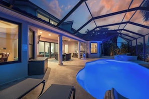A modern outdoor pool area with a glass ceiling, a dining area, and a view of the surrounding landscape. - Waterfront Fun, Pool & Spa Paradise with Game Room & Gulf Access - Palm Vista Villa - Roelens (Cape Coral)
