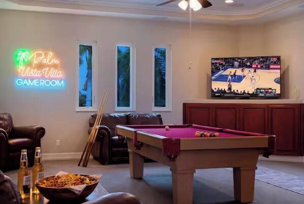 A pool table in a room with a neon sign, a television, and a pool cue rack. - Waterfront Fun, Pool & Spa Paradise with Game Room & Gulf Access - Palm Vista Villa - Roelens (Cape Coral)