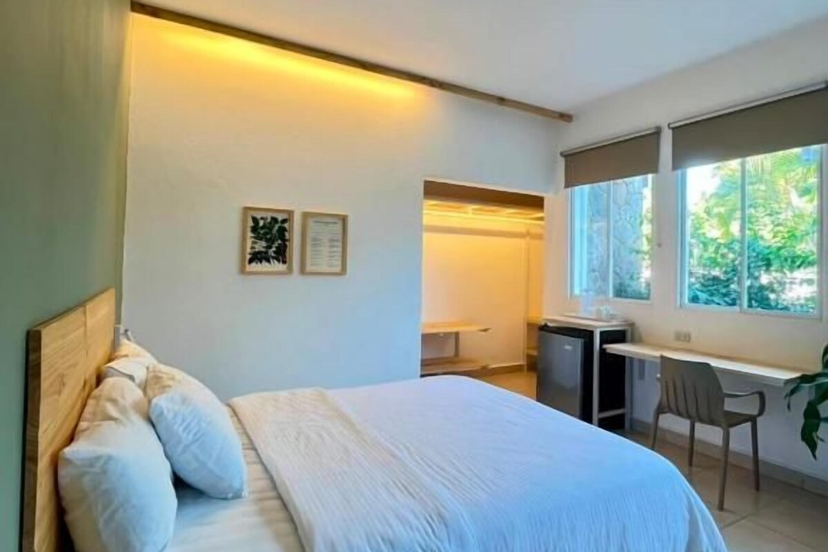 A bedroom with a bed, desk, chair, and a window.