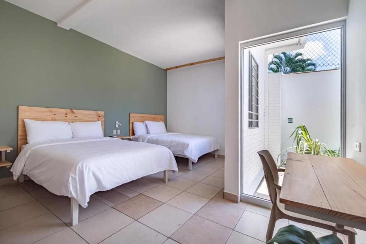 A bedroom with two beds, a wooden headboard, a bedside table, and a view through a glass door to the outside.
