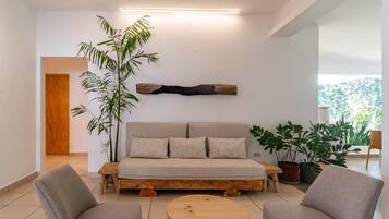 Un salon moderne comprenant un canapé, deux fauteuils, une table basse et une grande plante.