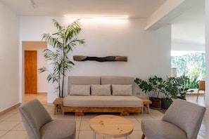 Uma sala de estar moderna com um sofá, duas poltronas, uma mesa de centro e uma planta grande.