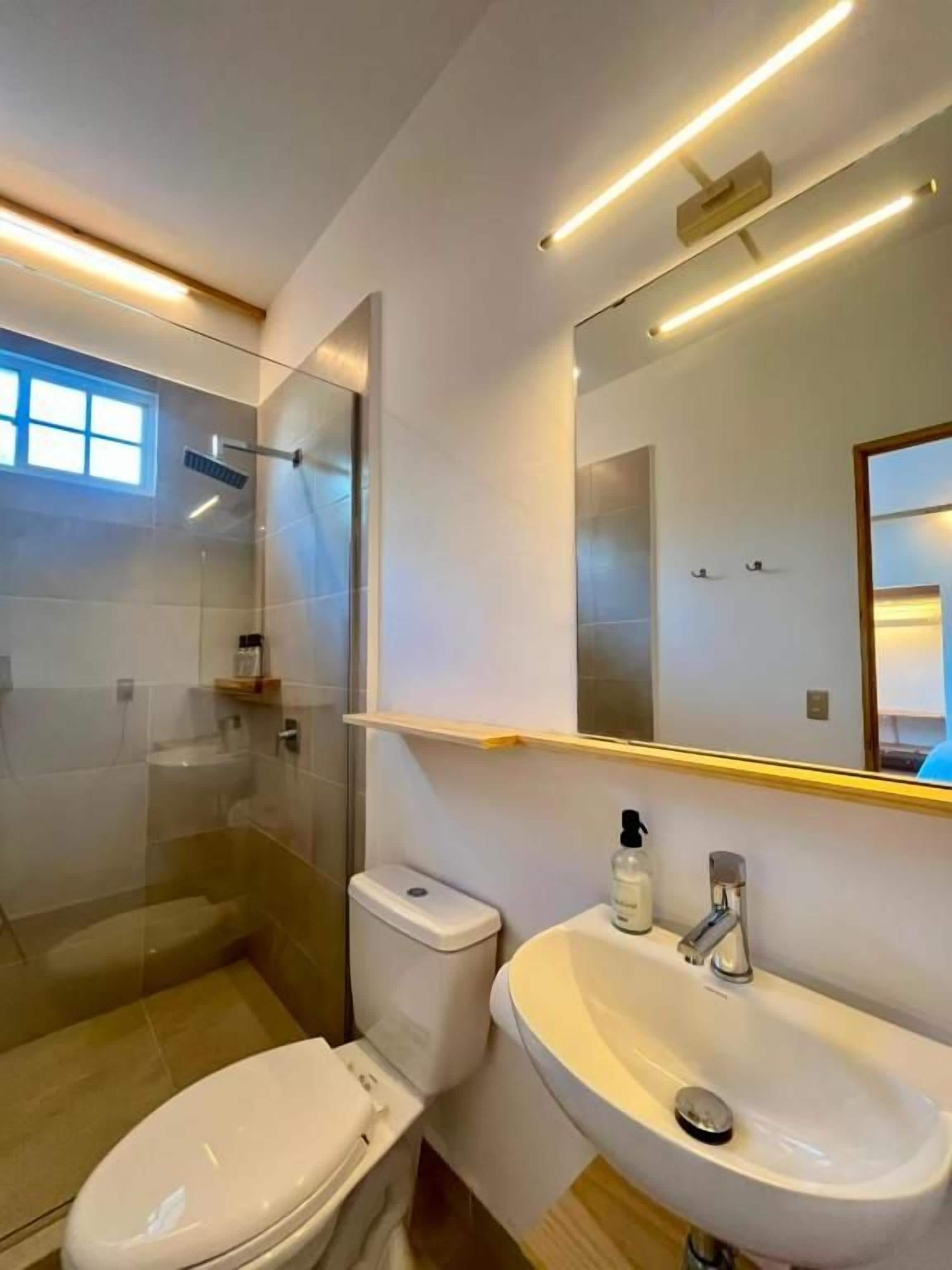 Ein modernes Badezimmer mit einer Duschkabine, einer weißen Toilette und einem weißen Waschbecken mit Spiegel darüber.