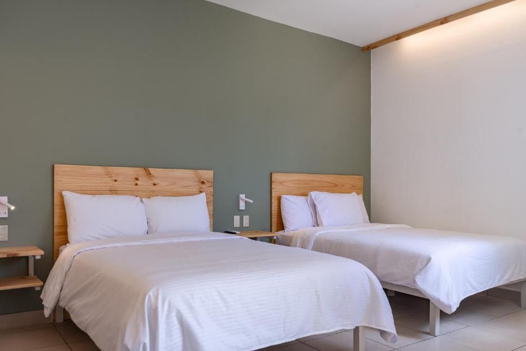 Habitación de hotel con dos camas individuales, cabeceros de madera, ropa de cama blanca y una mesita de noche pequeña con una lámpara.