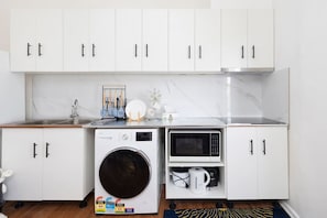 Een kleine keuken met een wasmachine, magnetron en koffiezetapparaat.