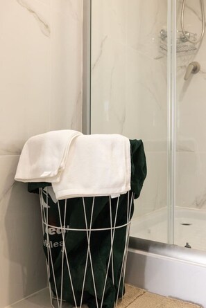 A laundry basket with a white towel and a green garment in a bathroom with a glass shower enclosure. - Sunnybank Hills Escape | 2BR Near Sunnybank Plaza (Sunnybank Hills)