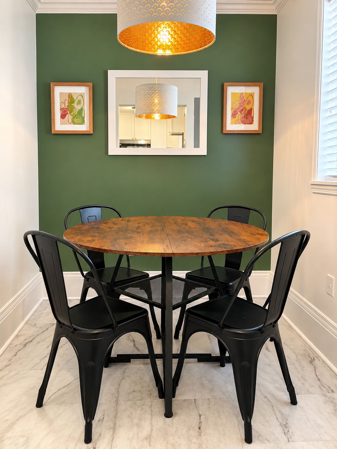 Un comedor con una mesa redonda de madera, sillas negras y una pared verde con obras de arte enmarcadas.