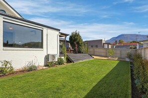 A residential property with a well-maintained lawn, a wooden deck, and a staircase leading to a covered area. - Spacious New Town Family Retreat (New Town)
