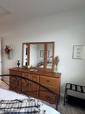 Een slaapkamer met een bed, een dressoir, een spiegel en een nachtkastje.