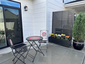 Een terras met een tafel en twee stoelen, een plantenbak met bloemen en een pot met een boom.