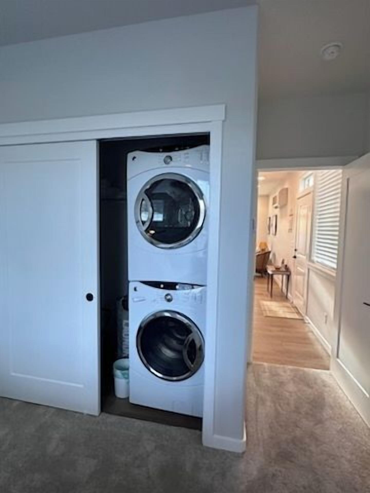 A laundry room with two stacked washers and dryers, a door leading to a hallway, and a carpeted floor.