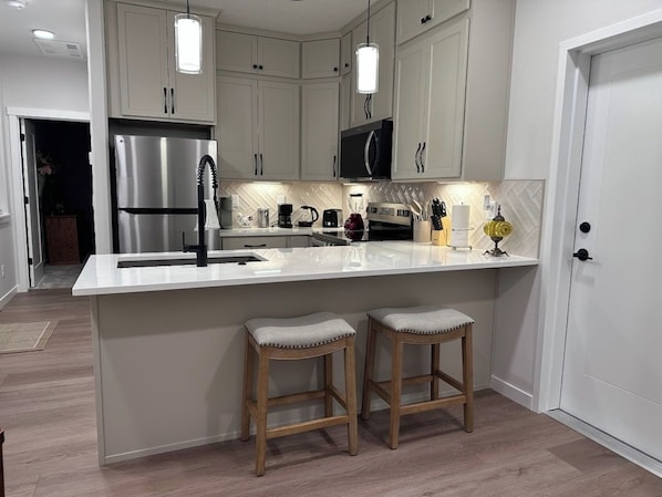 A modern kitchen with white cabinetry, stainless steel appliances, and two wooden stools.
