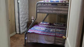 A bunk bed with patterned bedding, a single mattress against the wall, and a carpeted floor.