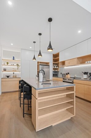 Une cuisine moderne dotée d’un îlot central, de luminaires suspendus et d’appareils électroménagers intégrés.