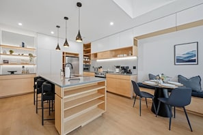 A modern kitchen with a central island, wooden cabinets, and pendant lighting. - 3-Story Designer Townhome by City Park (Manhattan)