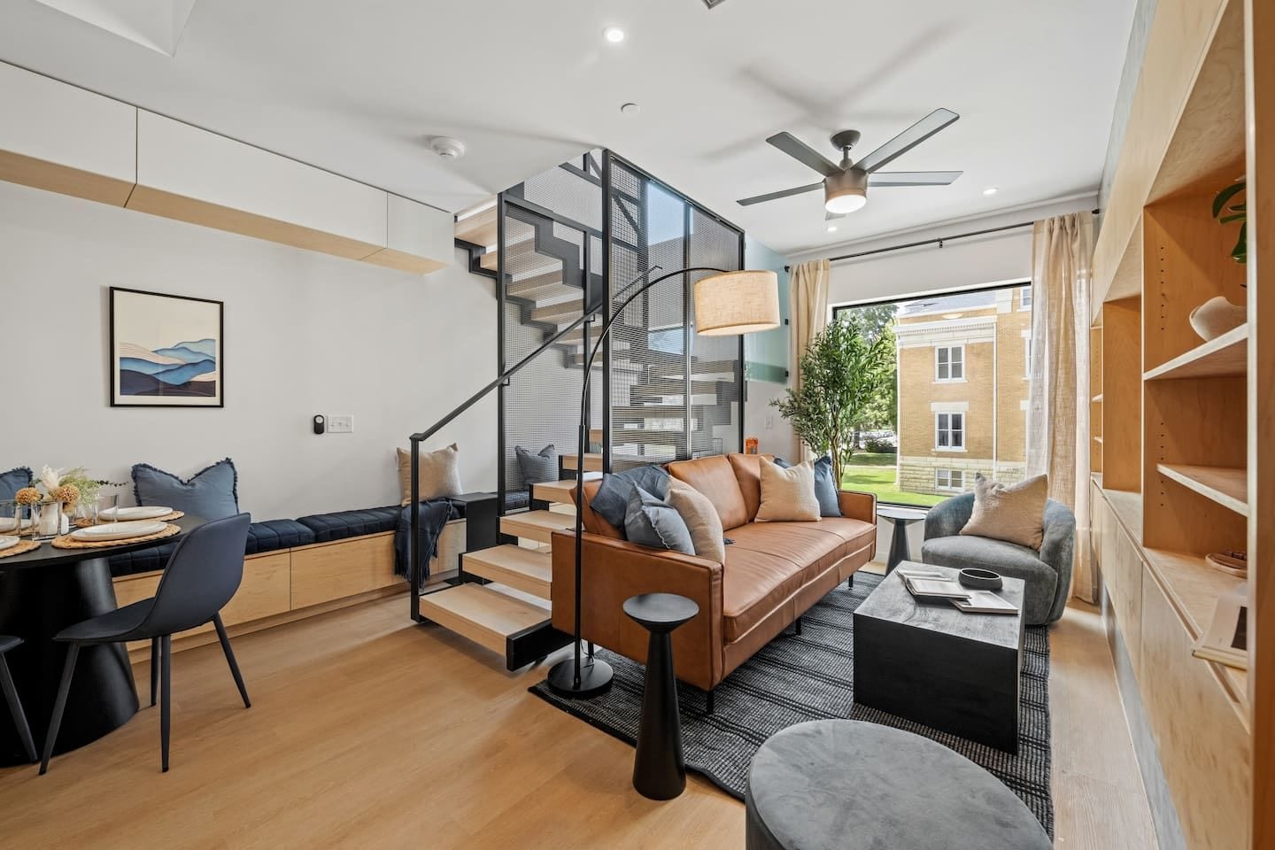 A modern living room with a staircase, a dining area, and a view of the outside.