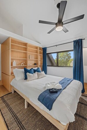 Une chambre à coucher comprenant un lit, un ventilateur de plafond, une fenêtre avec des rideaux et une armoire intégrée.
