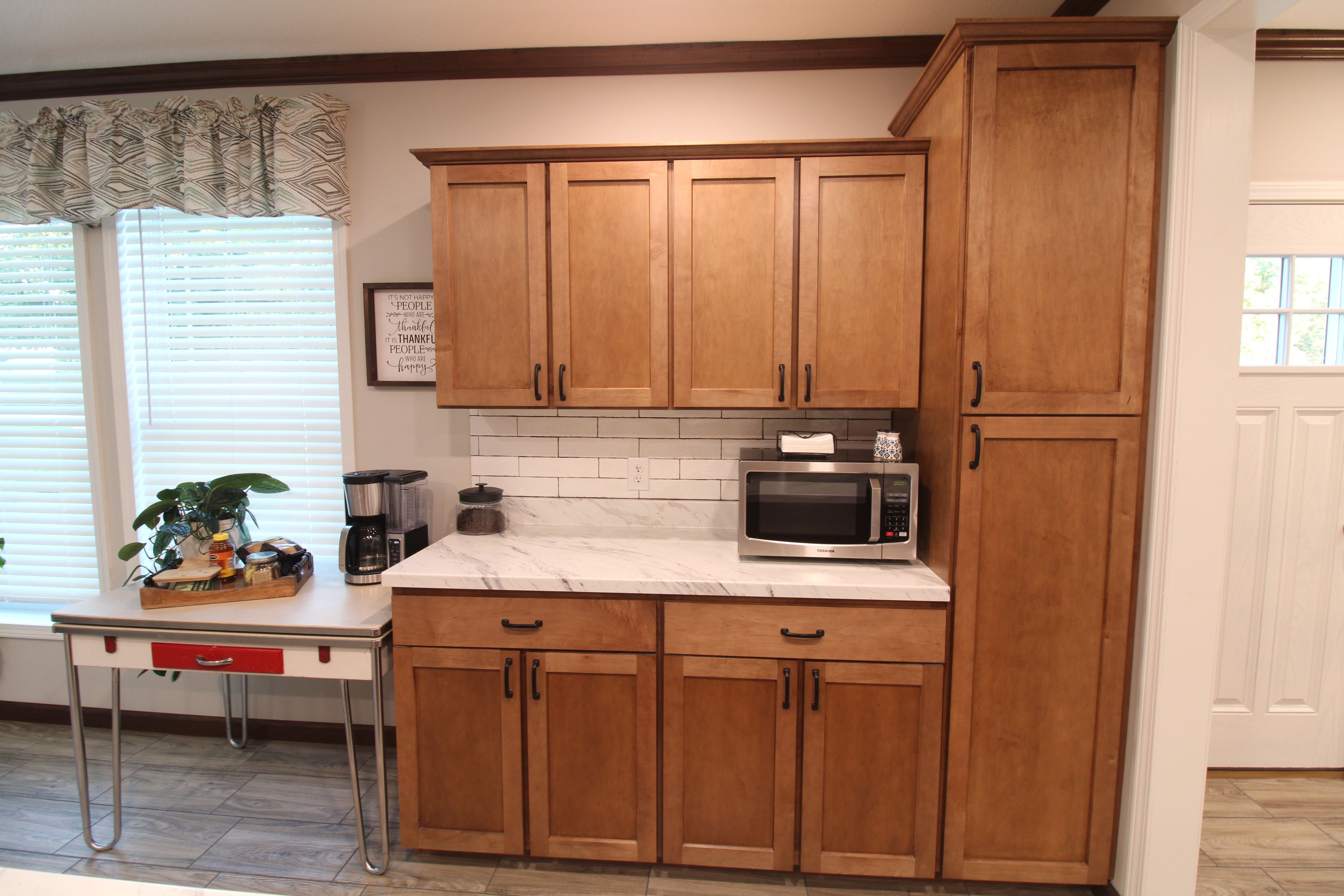 A kitchen with wooden cabinets, a microwave, a coffee maker, and a window with blinds.