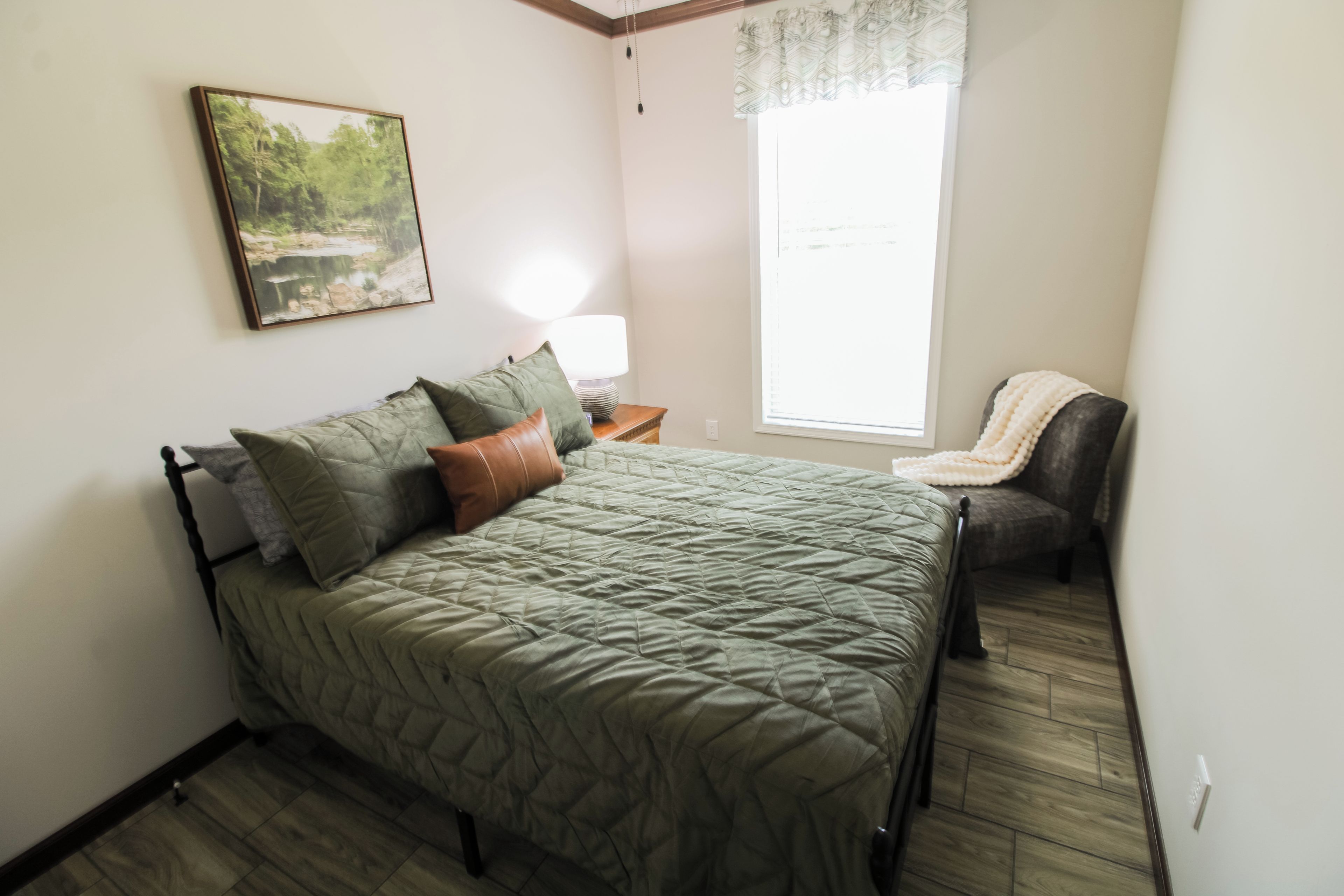 Quarto com cama, mesa de cabeceira, abajur, cadeira e janela.