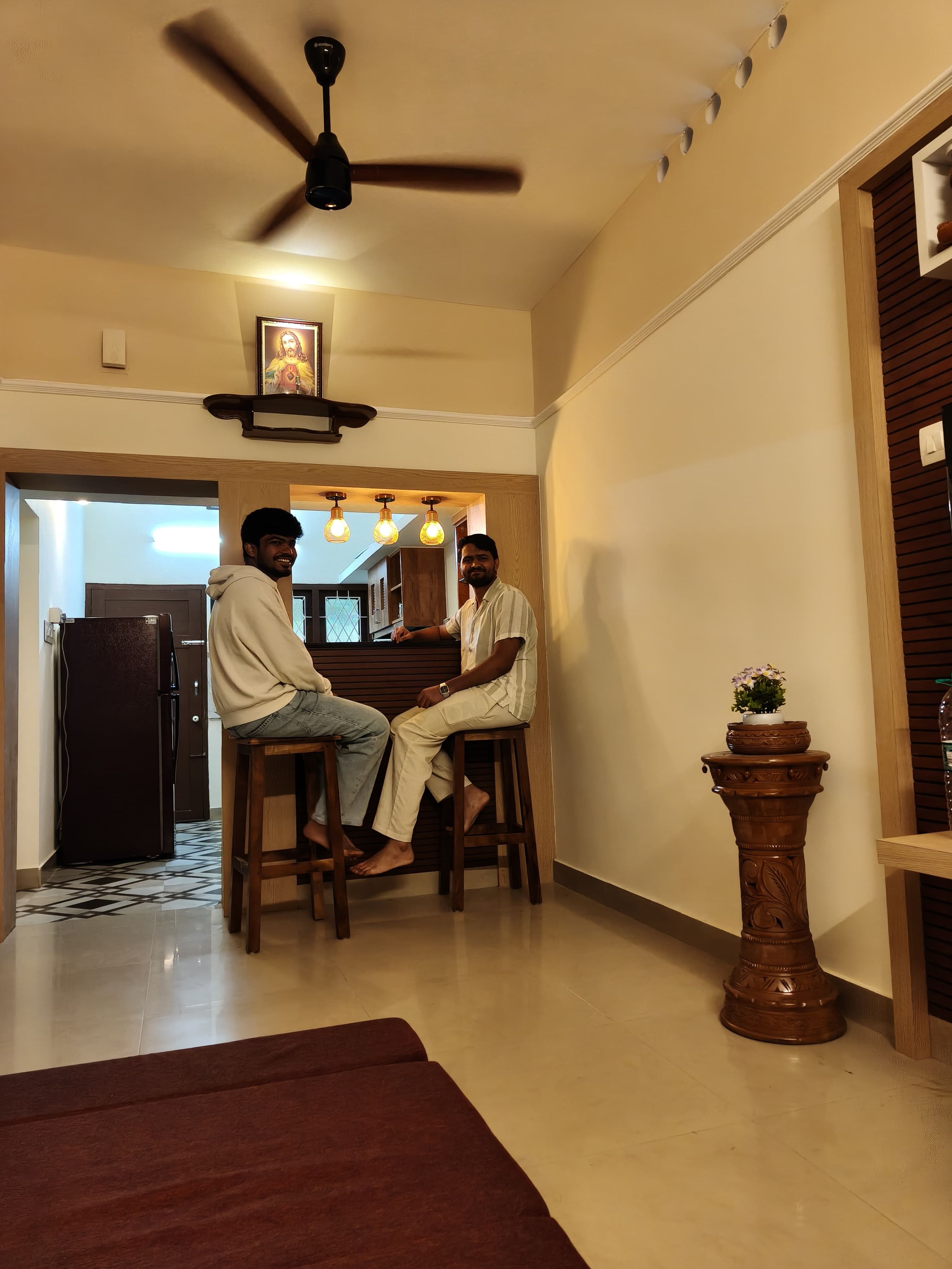 A room with a ceiling fan, a wooden table, and two people seated.