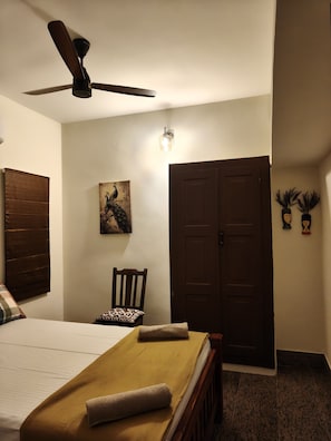A hotel room with a bed, a chair, a ceiling fan, a door, and a wall-mounted light fixture.