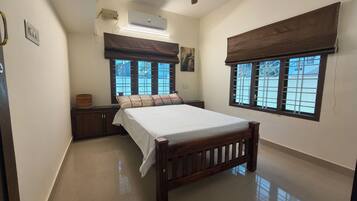 A bedroom with a bed, a nightstand, a window with a view, and an air conditioning unit.