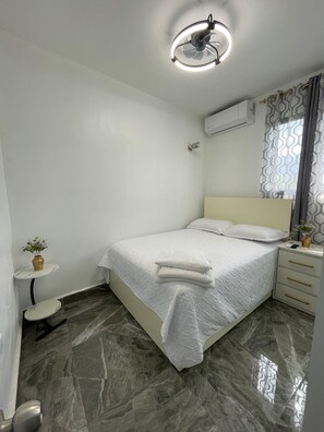 A bedroom with a bed, bedside tables, a small table with a vase, a ceiling fan, and an air conditioning unit. - 3-bedroom house in wonderful Bonao with big pool (Bonao)