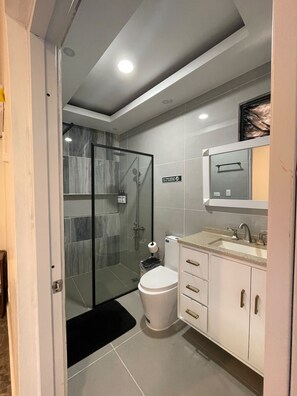 A modern bathroom with a glass shower enclosure, a toilet, and a sink with a mirror above. - 3-bedroom house in wonderful Bonao with big pool (Bonao)