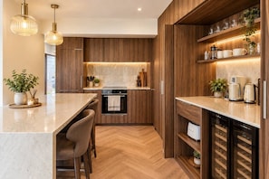 A modern kitchen with wooden cabinetry, a built-in oven, and a bar area with stools. - Casa Rossa Lux 2-bedroom Apartment in Sea Point (Cape Town)