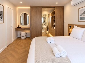 Une chambre d’hôtel avec un grand lit, une armoire en bois, une salle de bain avec un miroir et une vue sur la mer.