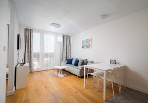 A modern living room with a sofa, a dining table, and a TV. - Park Mirowski Skyline Apartment (Warszawa)