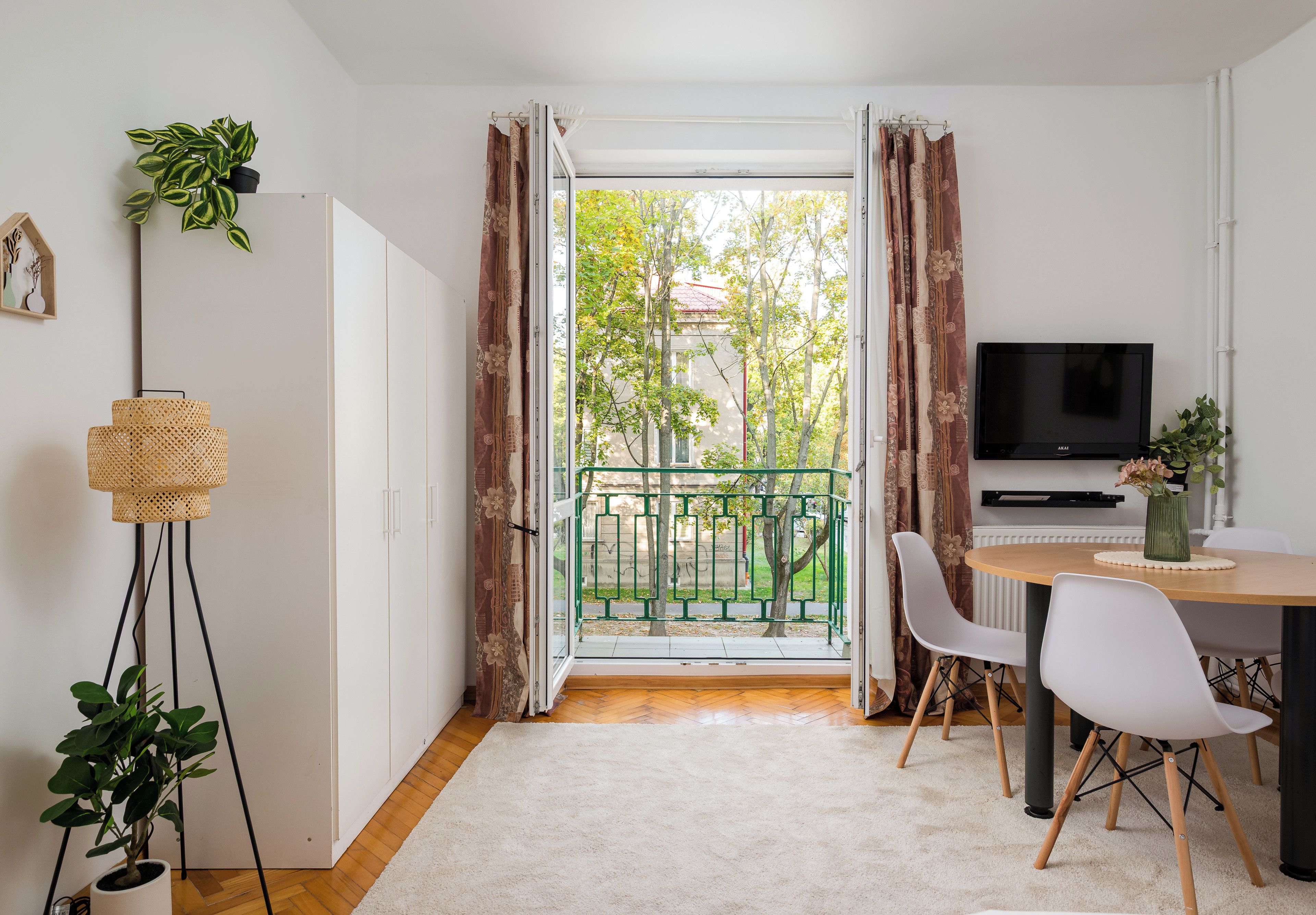 Ein modernes Wohnzimmer mit Fernseher, Essbereich und Blick auf einen begrünten Balkon.