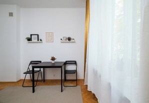 A minimalist dining area with a table, chairs, and two wall-mounted shelves with decorative items. - Gruszczyńskiego Classic Apartment (Warszawa)