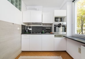 A modern kitchen with white cabinets, a built-in oven, and a window with a view of trees. - Gruszczyńskiego Classic Apartment (Warszawa)
