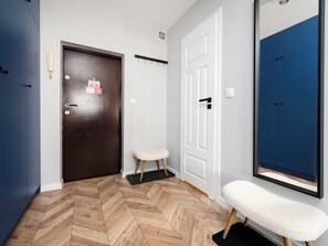 A hallway with a wooden herringbone floor, a dark brown door with a sign, a white door with a black handle, and a blue cabinet. - Wółczańska Central Studio (Łódź)