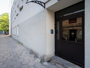 A building with a black door, a small window with a keypad, and a wall-mounted light fixture. - Wółczańska Central Studio (Łódź)