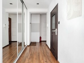 A hallway with wooden flooring, a glass door, a dark wooden door, and a white wall with a light switch. - Księży Młyn Loft Studio (Łódź)