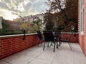 A balcony with a brick wall, a table with chairs, and a view of houses and trees. - Poniatowskiego Signature Apartment (Wrocław)