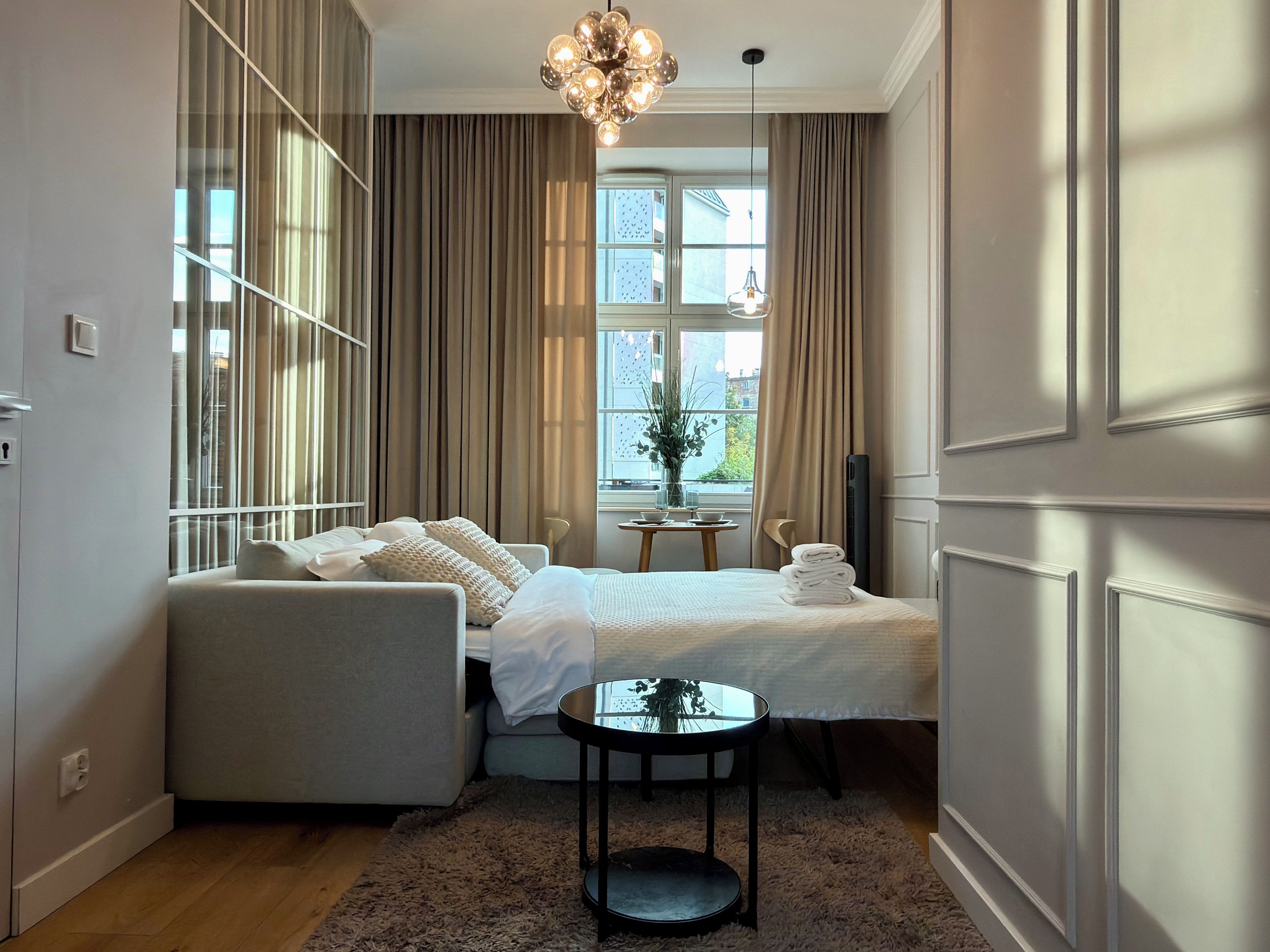 Una habitación de hotel con una cama, un sofá, una mesita y una ventana con cortinas.