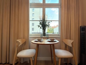 A room with a table and two chairs, a window with curtains, and a vase with plants. - Poniatowskiego Signature Apartment (Wrocław)