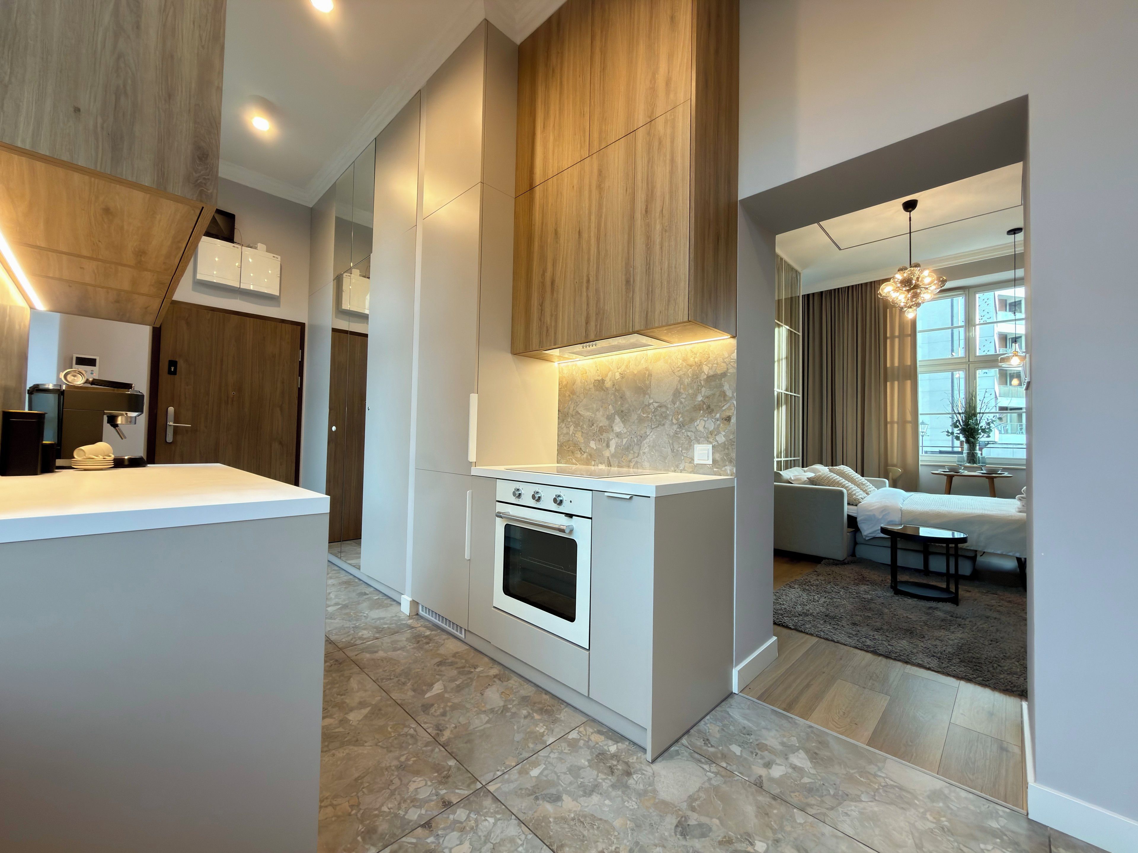 A modern kitchen with a built-in oven, a coffee machine, and a dining area with a sofa and table.