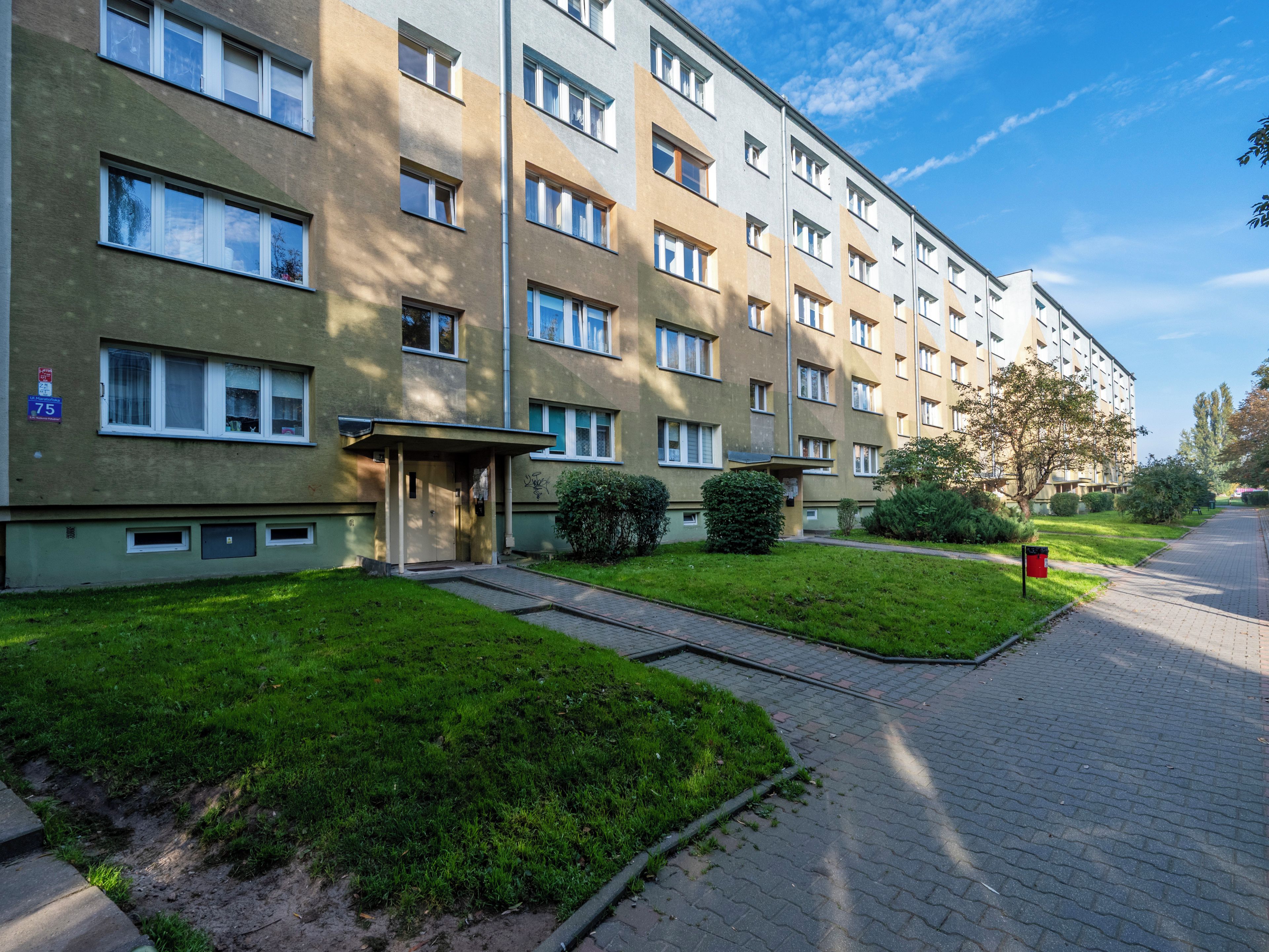 A multi-story residential building with a flat facade, rectangular windows, and a small entrance area with a door.