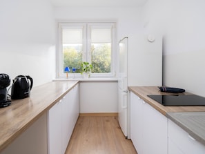 A compact kitchen with white cabinets, a wooden countertop, a black kettle, a blue lamp, and a potted plant. - Maratońska Standard Apartment (Łódź)