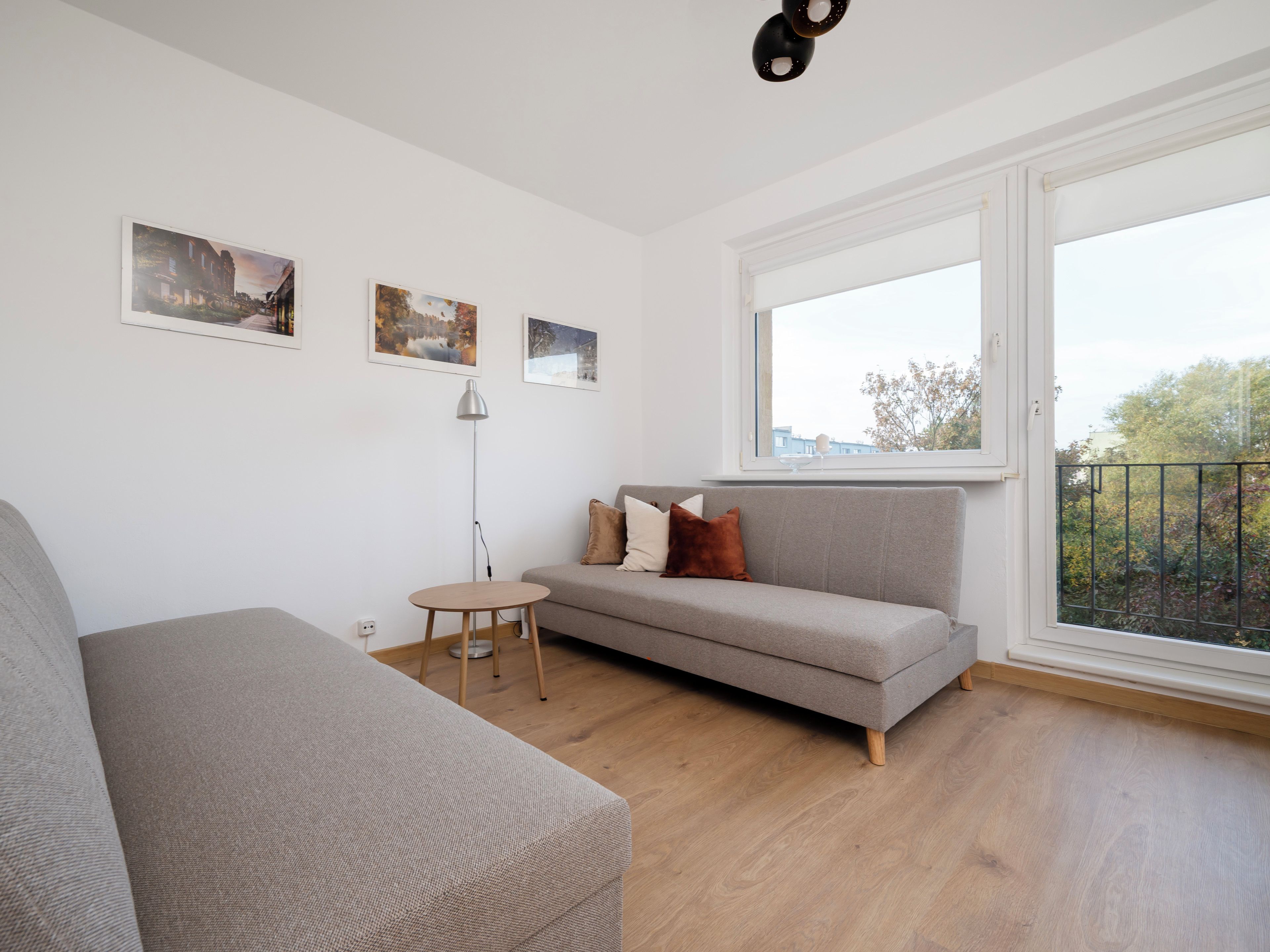 A modern living room with a grey sofa, a round wooden table, and three framed pictures on the wall.