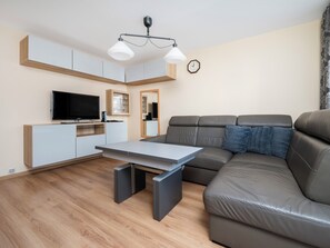 Ein modernes Wohnzimmer mit Flachbildfernseher, einer Couch, einem Esstisch und einer Deckenleuchte.