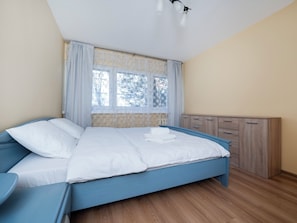 Ein Schlafzimmer mit Bett, Fenster mit Vorhängen, Nachttisch und Kleiderschrank.