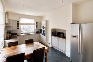 A modern kitchen with white cabinetry, a wooden dining table, and a stainless steel refrigerator. - Cosy Victorian Home in Levenshulme's Trendy Suburb (Manchester)