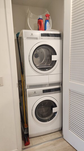 Eine Waschmaschine mit Frontlader, eine Bedarfsanzeige, ein Mop und Reinigungsmittel im Hauswirtschaftsraum.