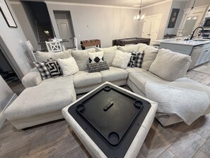 A modern living room with a sectional sofa, a pool table, and a kitchen area in the background. - Edmond 4BR Entertainment Retreat, Pool Table, Air Hockey, Ping Pong & Sleeps 10 (Edmond)